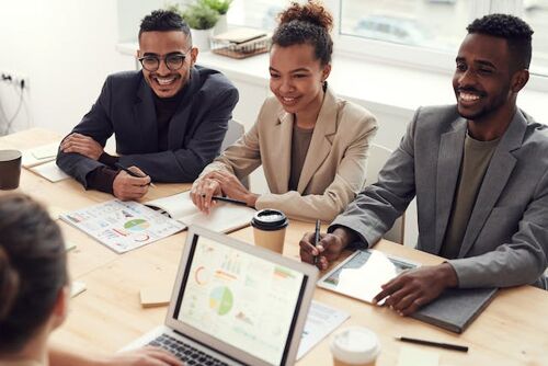 Three smiling people are sitting at the table and talking with a colleague in the office