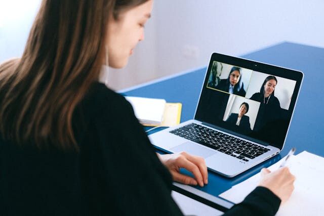 A woman in a black shirt talking to three other people via zoom.