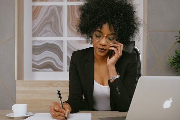 A woman taking on the phone while writing on paper.