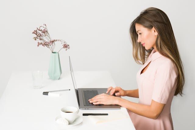 A woman in a pink dress working on her laptop